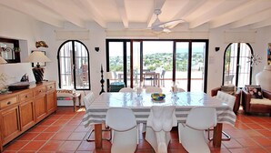 A dining area with a large table, white chairs, and a view through large windows. - Argentario - sea view villa with private pool in Benissa (Benissa)
