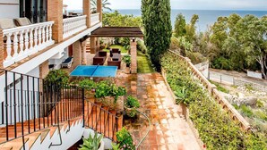 Una casa de dos pisos con un patio, mobiliario exterior y vista al mar.
