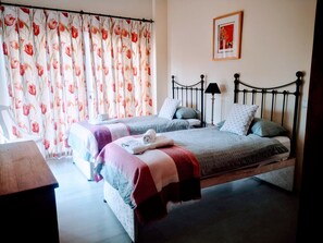 Un dormitori amb dos llits, cortines florals, un quadre al mur i una làmpada de nit.
