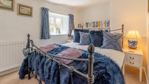 A bedroom with a bed, a nightstand, a lamp, a window with curtains, and a bookshelf. - Forsythia Cottage - sleeps 3 guests  in 2 bedrooms (Bourton-on-the-Water)