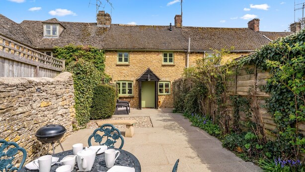 A stone cottage with a green door, a patio with outdoor seating, and a stone wall. - Forsythia Cottage - sleeps 3 guests  in 2 bedrooms (Bourton-on-the-Water)