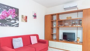 Un salon avec un canapé rouge, un téléviseur et un meuble en bois doté de portes en verre.