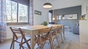 Un comedor moderno con una mesa y sillas de madera, una lámpara colgante y vistas al exterior a través de amplios ventanales.