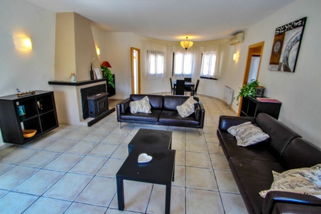 A living room with a sofa set, a coffee table, and a fireplace. There is a dining area with a table and chairs visible in the background.