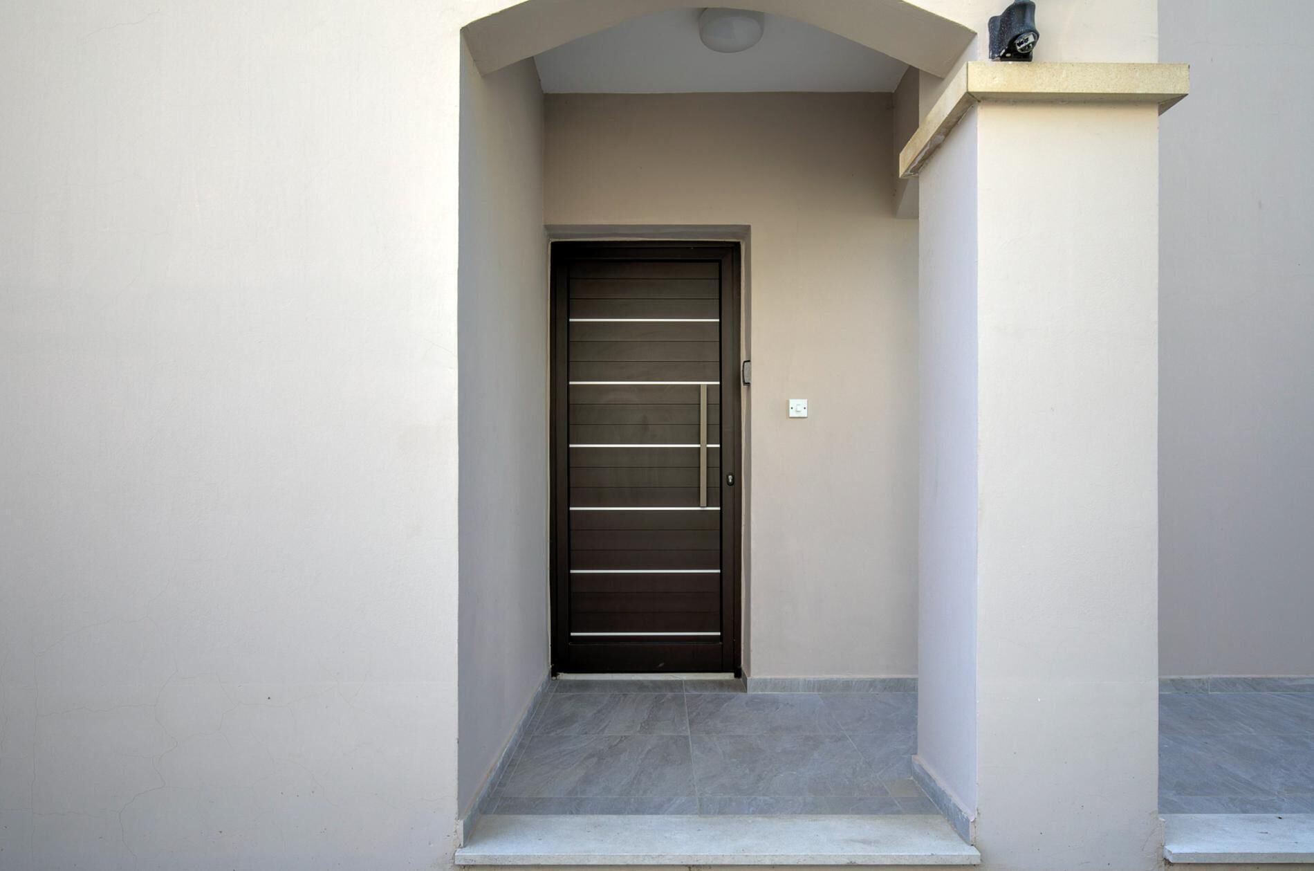 Un ingresso moderno con una porta scura, un piccolo gradino e una parete chiara.
