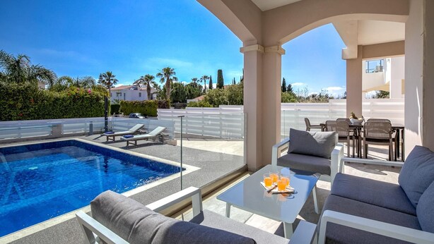 A poolside area with lounge chairs, a table with drinks, and a view of the pool and surrounding landscape. - Villa Crystal by Ezoria Villas (Coral Bay)