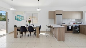 A modern kitchen with a central island, a dining area with chairs, and a view of the outside. - Villa Crystal by Ezoria Villas (Coral Bay)