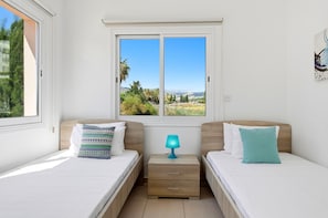 A bedroom with two beds, a window with a view, a nightstand, and a lamp.