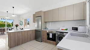 A modern kitchen with a central island, a built-in washing machine, and a microwave. - Villa Crystal by Ezoria Villas (Coral Bay)
