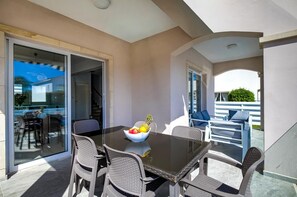 Un balcone con una porta vetrata che dà su un ambiente interno, un tavolo con sedie e una ciotola di frutta.