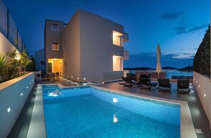 Um edifício moderno com piscina no terraço, espreguiçadeiras e vista para o mar ao entardecer.