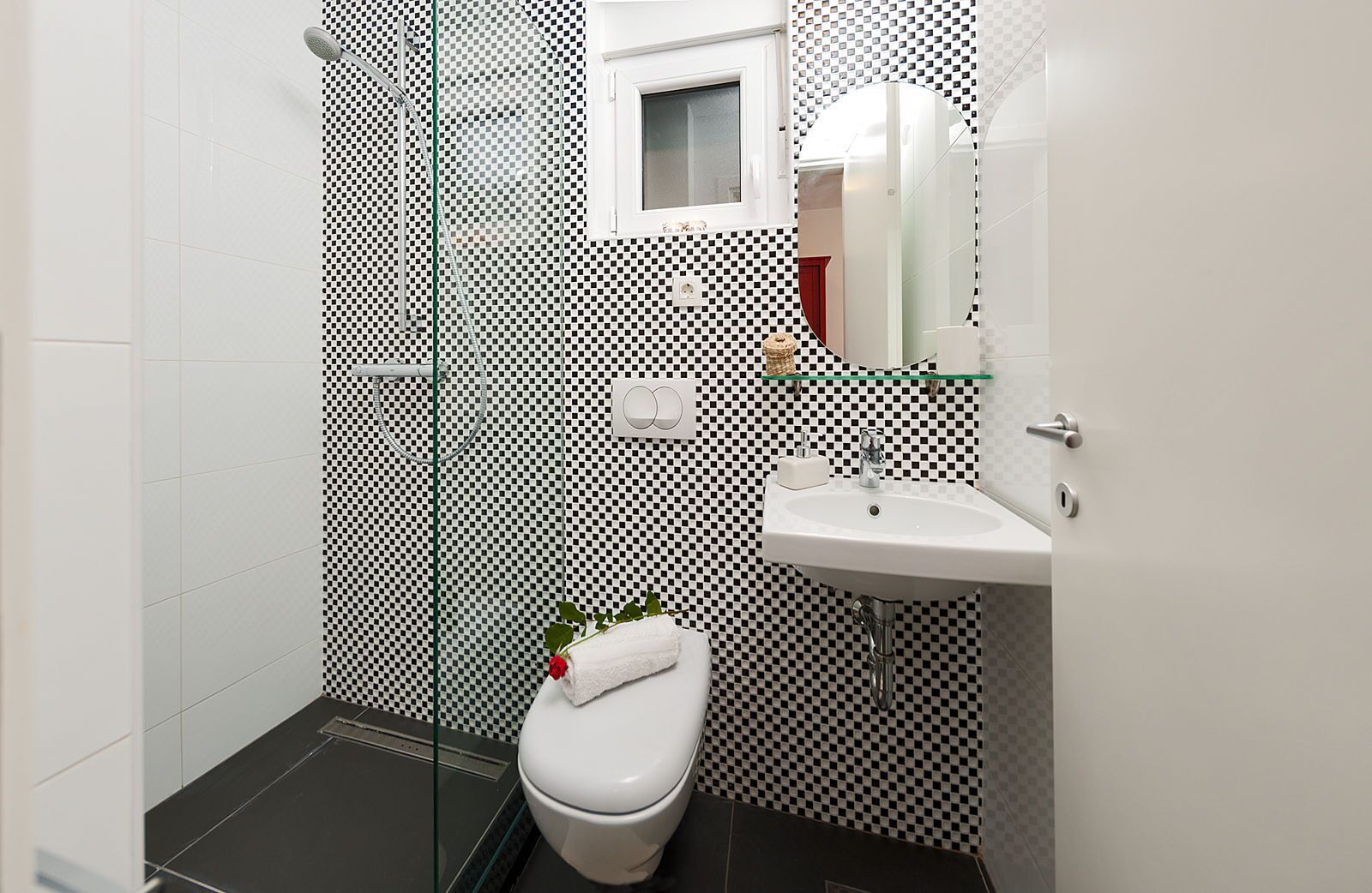 A modern bathroom with a checkered wall pattern, a glass shower enclosure, a white toilet, and a sink with a mirror above it.
