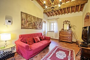 A living room with a red sofa, a wooden dresser, a chandelier, and a large painting on the wall.