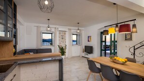 Eine moderne Küche mit einer Holzinsel, ein Essbereich mit Tisch und Stühlen sowie eine Wohnbereich mit Sofa und Fernseher.
