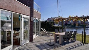 Un patio exterior con una mesa y sillas, un acceso por puerta de vidrio y vista al río.
