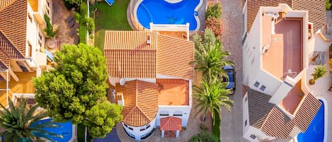 Vista aérea de una zona residencial con dos piscinas, un árbol grande y un jardín bien cuidado.