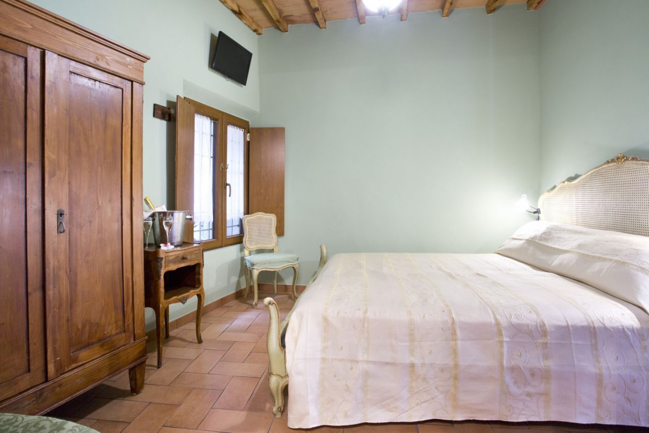 Une chambre à coucher comprenant un lit, une armoire en bois, un bureau avec une chaise et un téléviseur fixé au mur.