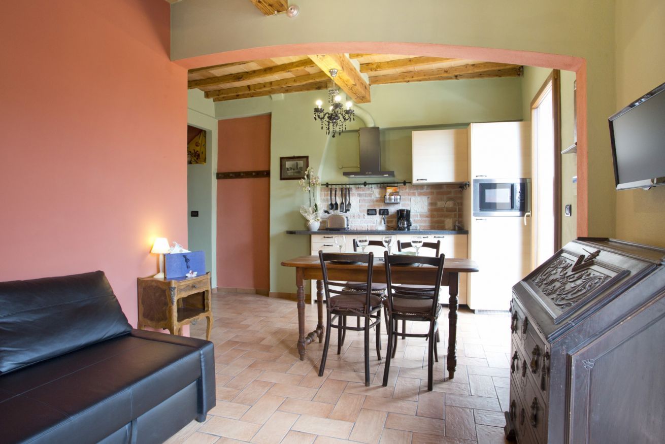 Un salon chaleureux avec un canapé, une table à manger et des chaises, un buffet en bois, et une cuisine en arrière-plan.