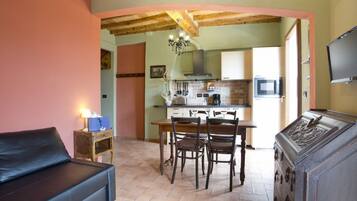 Un salon chaleureux avec un canapé, une table à manger et des chaises, un buffet en bois, et une cuisine en arrière-plan.