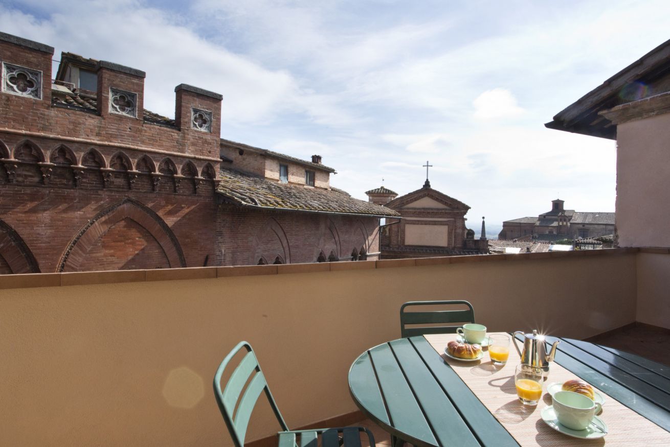 Un balcon avec une table dressée pour le petit-déjeuner, offrant une vue sur des bâtiments historiques à l’architecture remarquable.
