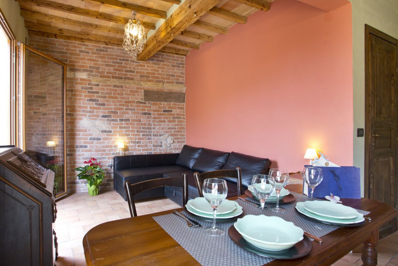 A dining area with a wooden table set for four, a brick wall, a leather sofa, and a chandelier.
