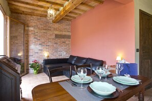 A dining area with a wooden table set for four, a brick wall, a leather sofa, and a chandelier.