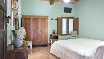 Ein Schlafzimmer mit einem Holzschrank, einem Bett mit weißer Bettdecke, einem kleinen Tisch mit Blumenvase und einem Fenster mit Vorhängen.