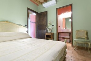 A bedroom with a large bed, a wooden door, a vanity with a mirror, and a chair.