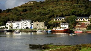 A coastal town with a prominent white building, a stone structure, and a hill with a tower.