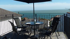 A balcony with a table and chairs, a large umbrella, and a view of the ocean. - The Salt Pot -  a cottage that sleep 6 guests  in 3 bedrooms (Ventnor)