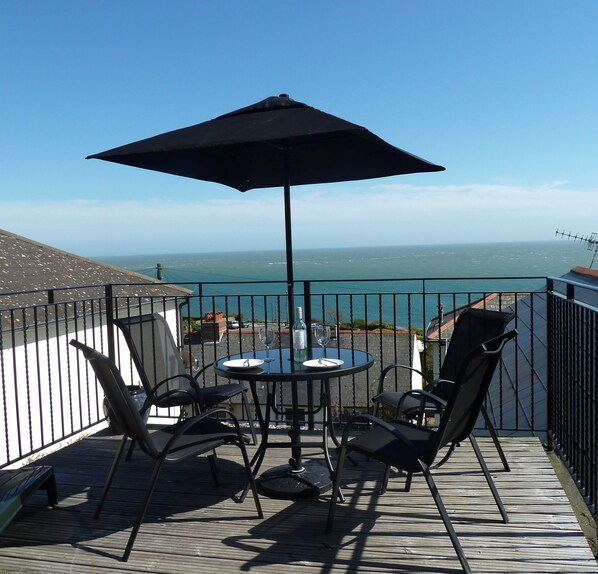 A balcony with a table and chairs, a large umbrella, and a view of the ocean.