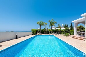 A swimming pool with a clear view of the ocean, surrounded by palm trees and lounge chairs. - Villa Cassia by Ezoria Villas (Coral Bay)