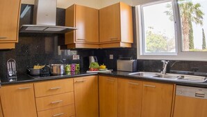 A kitchen with wooden cabinets, a black countertop, a window with a view of palm trees, and a dishwasher. - Villa Casa Mia by Ezoria Villas (Coral Bay)