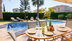 A poolside dining area with a table set for two, a pool, and lounge chairs. - Villa Casa Mia by Ezoria Villas (Coral Bay)