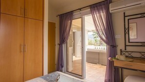 A bedroom with a bed, a desk, and a wardrobe. There is a sliding glass door leading to an outdoor area. - Villa Casa Mia by Ezoria Villas (Coral Bay)