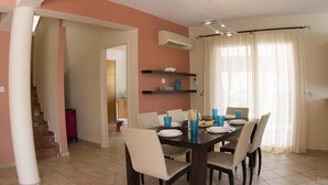 A dining area with a table set for four, chairs, a staircase, and a wall-mounted shelf with decorative items. - Villa Casa Mia by Ezoria Villas (Coral Bay)