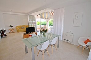 Een moderne woonkamer met een glazen eettafel, witte stoelen, een bank en een televisie.