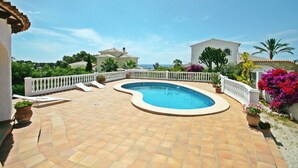 Ein Pool mit geschwungener Kante, umgeben von einem weißen Zaun und Topfpflanzen.
