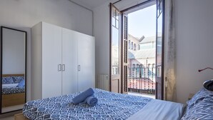 Een slaapkamer met een bed, een kledingkast en een balkon met uitzicht op gebouwen.