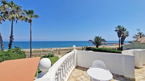 A balcony with a white chair and table, overlooking a beach with palm trees and a clear blue sky. - Villa Charlie - Denia, Costa Blanca (Denia)