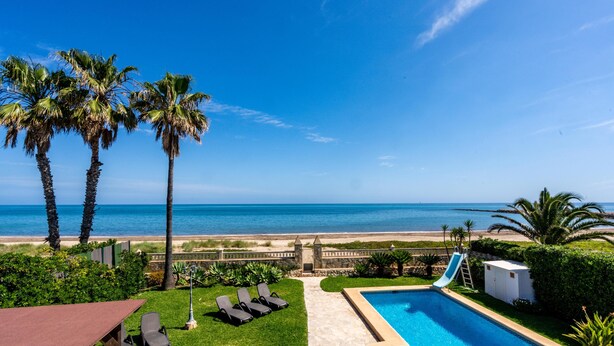 A pool with a slide, palm trees, and a view of the beach. - Villa Charlie - Denia, Costa Blanca (Denia)