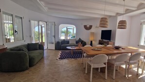 A spacious living area with a wooden dining table, comfortable seating, a television, and large windows with decorative grills. - Villa Charlie - Denia, Costa Blanca (Denia)