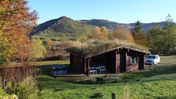 A rustic cabin with a thatched roof, a small outdoor seating area, and a car parked nearby.