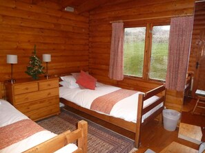 A wooden cabin bedroom with a bed, dresser, and a small Christmas tree. - Log Cabin with Hot Tub | Sleeps 4 | In the Cairngorm National Park | Accepts Dogs (Spittal of Glenshee)
