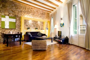 A living room with a stone wall, wooden flooring, a sofa, a coffee table, and a television. - Picasso Apartment - One Bedroom Apartment, Sleeps 2 (Barcelona)