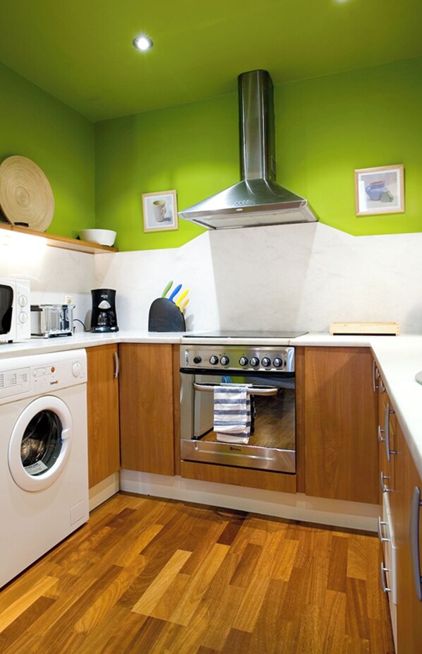 A compact kitchen with a washing machine, a stove, and a microwave.