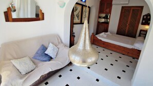 Ein Zimmer mit einer Couch, einer Hängelampe, einem Bett und einem Spiegel an der Wand.