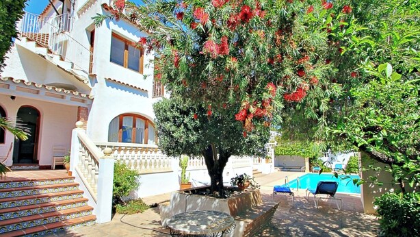 Ein Innenhof mit Pool, ein Baum mit roten Blüten, eine Treppe und eine Liegefläche am Pool.