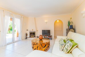 A living room with a white sofa, a round coffee table, a fireplace, a television, and a sliding glass door.