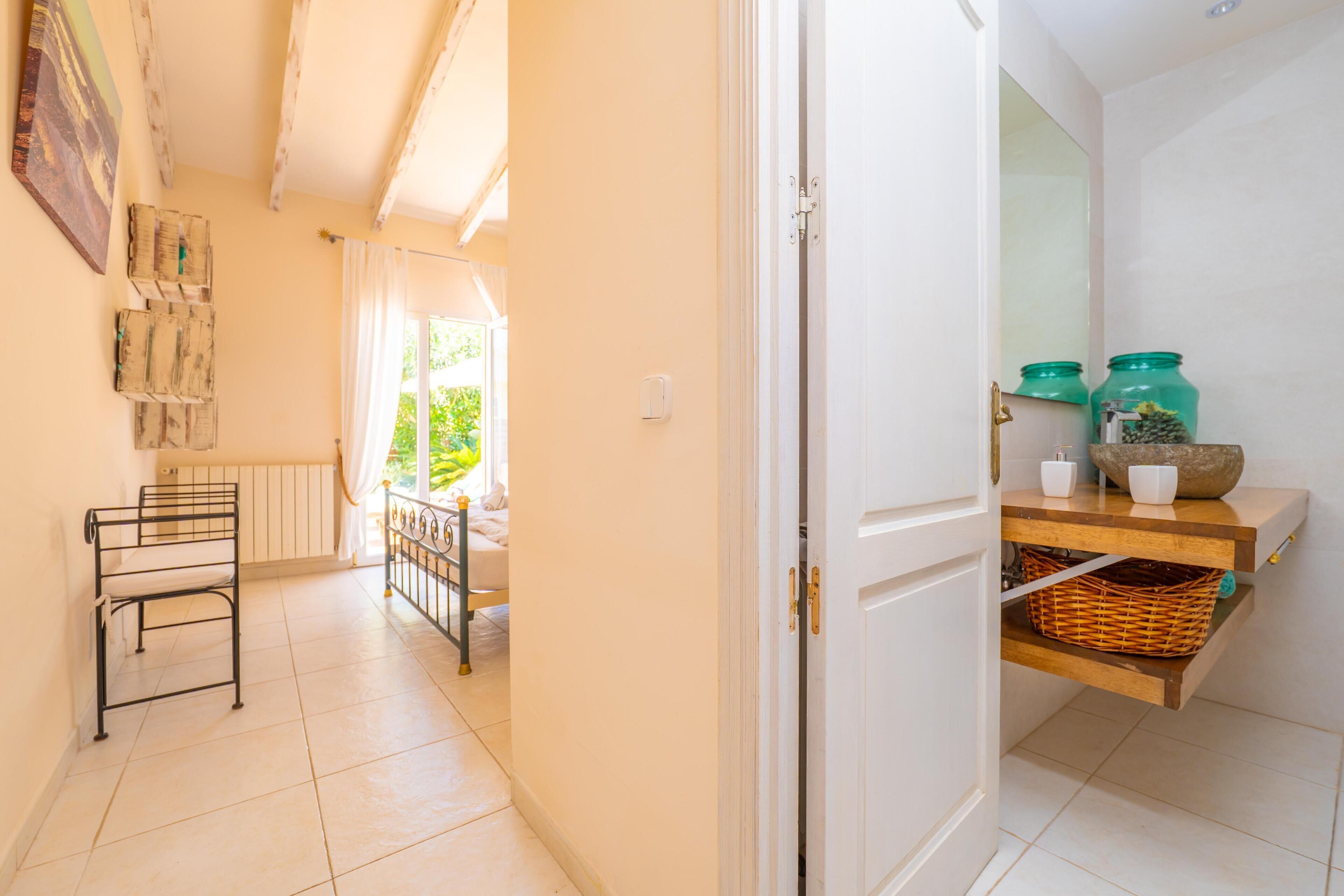 Un pasillo con un perchero metálico, una puerta que da a una habitación con ventana, y una repisa con frascos y una cesta.
